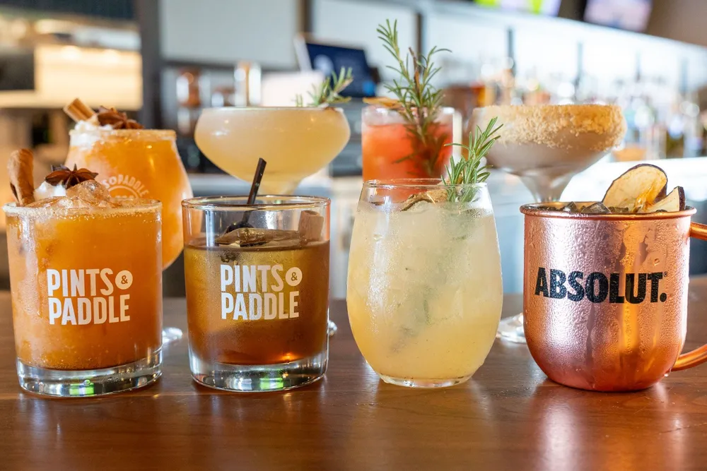 The seven fall drinks lined up on the walnut bar: the Pumpkin Pie Smash, Orchard Old Fashioned, Sweater Weather Spritz and Autumn Mule in front, the Pear Martini, No Pear Pressure and Pumpkin Pie Espresso Martini behind.