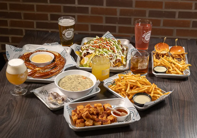 A spread of pretzel with beer cheese, nachos, sliders, fries and cheese curds with drinks