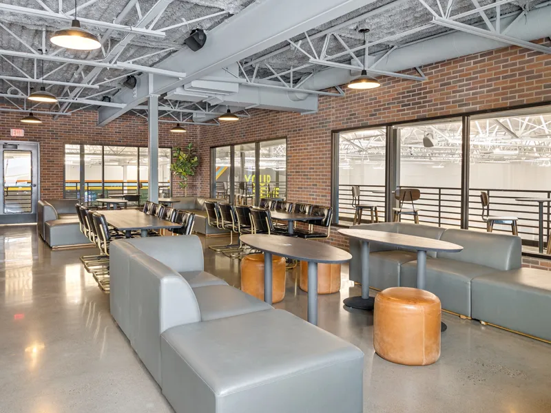 North mezzanine lounge with grey sofas, leather ottomans and a long table, windows overlooking the courts