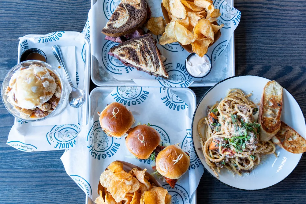 An overhead spread of the fall chef specials: a pastrami sandwich with kettle chips, three sliders, short rib bucatini pasta and peach cobbler with vanilla ice cream.