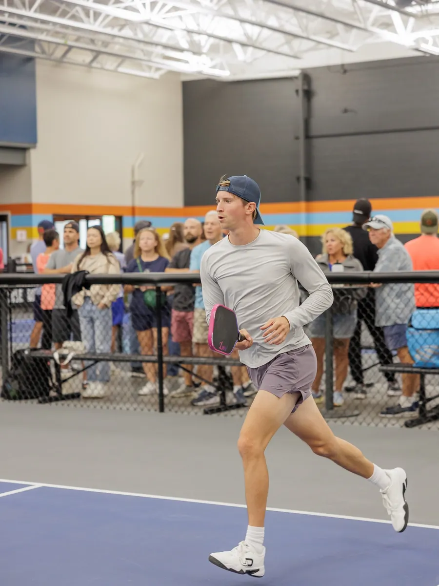 A player sprinting across an indoor court while spectators watch from the mezzanine