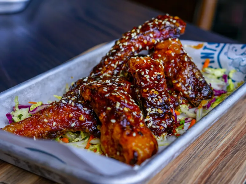 Glossy sesame-topped sticky ribs piled over slaw in a metal tray lined with branded paper